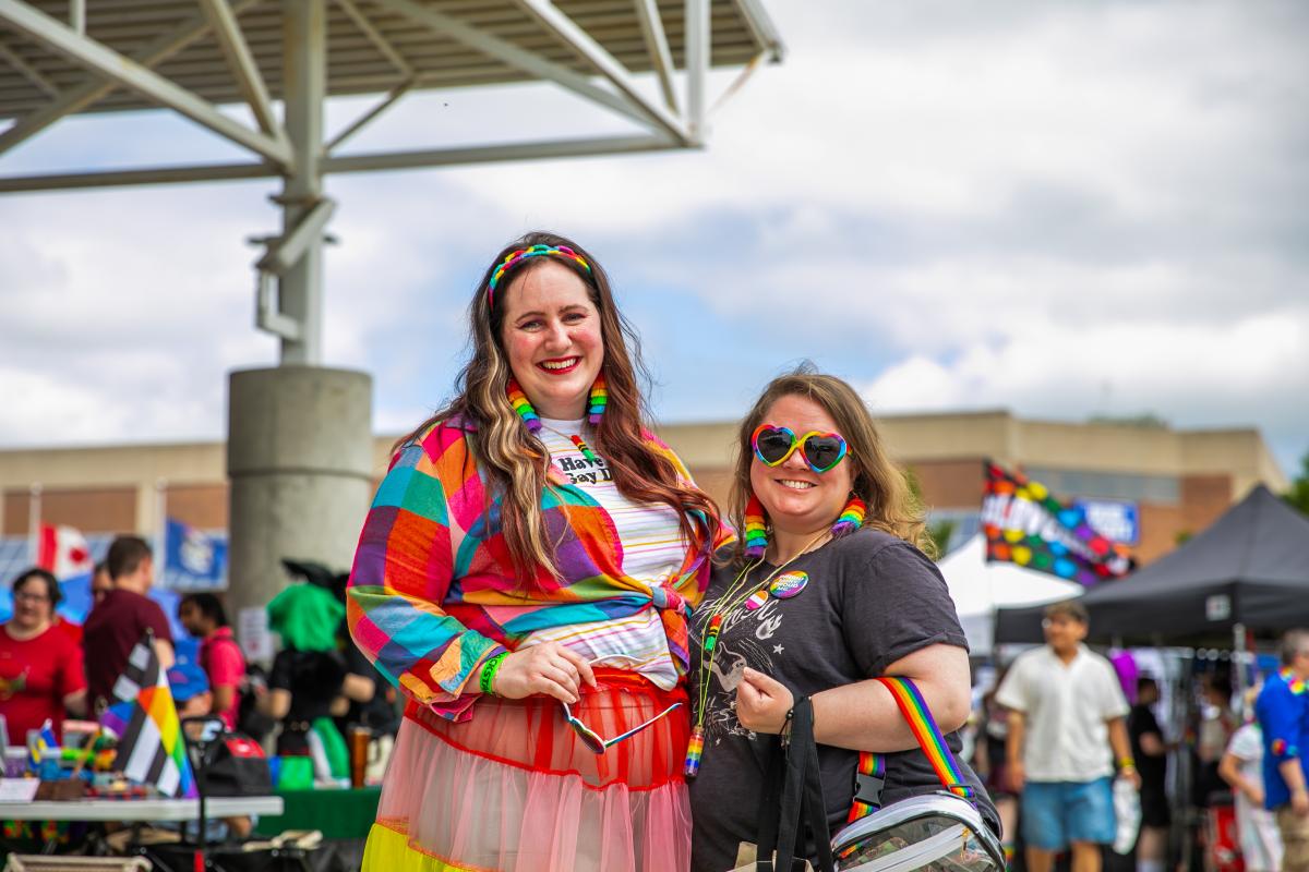 Two people in rainbow outfits embracing and smiling toward the camera.