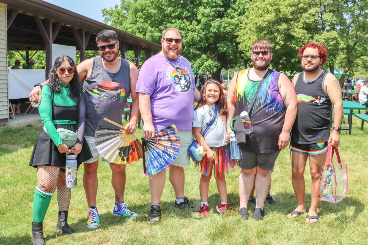 A group of six people at Mount Pleasant Pride Festival lined up and smiling toward the camera with hand fans.
