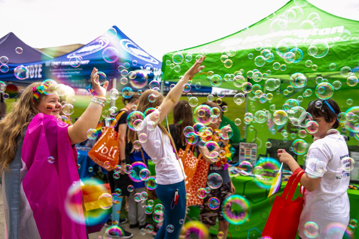 Children at the Great Lakes Bay Pride Festival playing with bubble machines, with bubbles filling the frame.