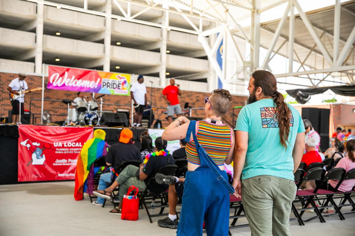 Two people watching the Great Lakes Bay Pride Festival performers on stage from the back of the seating area.