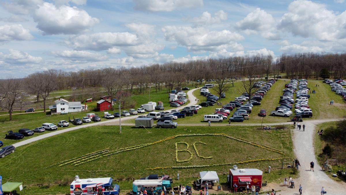Aerial view of hillside parking rows with daffodils spelling 'BC' on the lawn and food trucks near the entrance.
