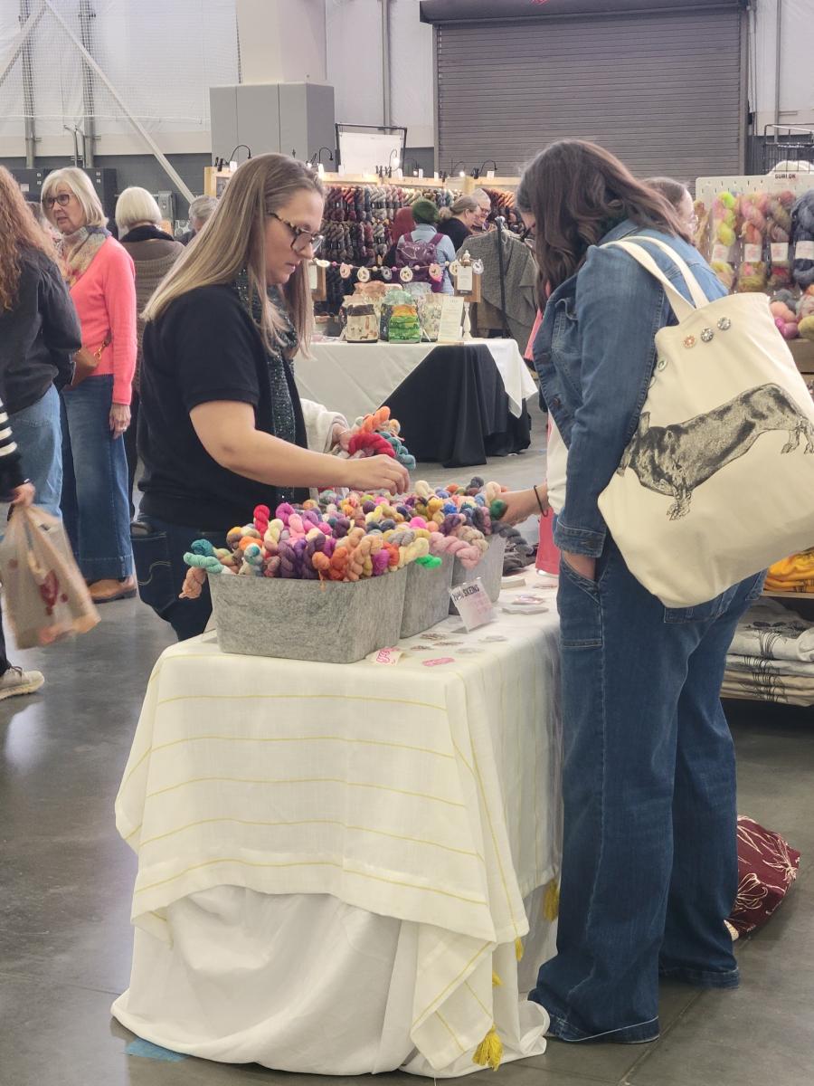 two women shopping for small skeins of yarn at a booth