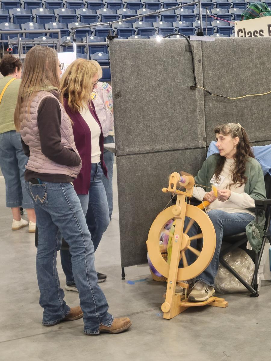 two women watching another women using a spinning wheel