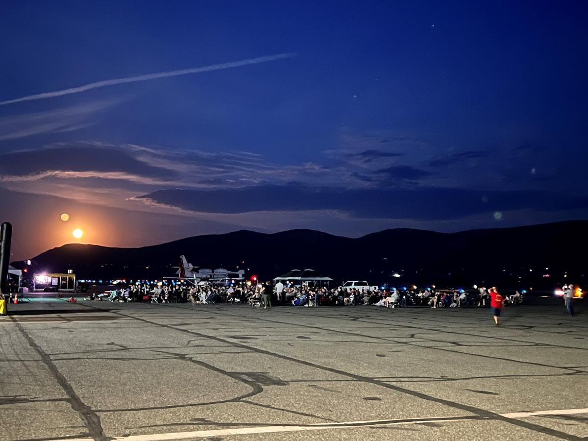 Crowd, at night, sitting in lawn chairs watching a movie on an inflatable screen at Pangborn Airport.