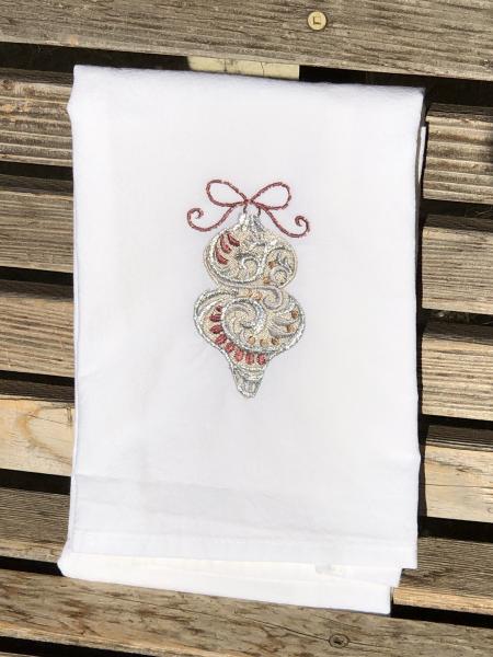 A Christmas ornament is embroidered on a white flour sack tea towel, dish towel, cotton