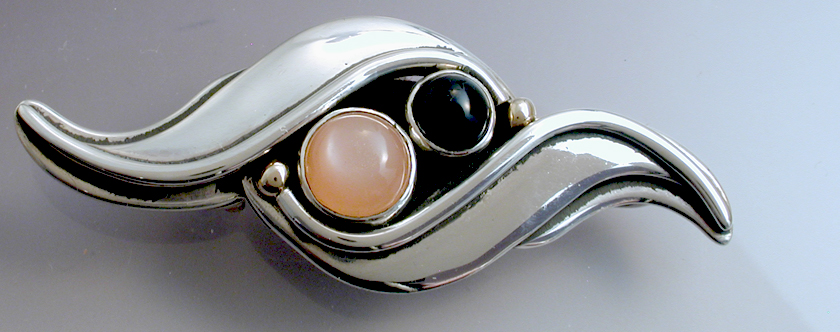 A silver pin/pendant with black onyx and peach colored moonstone picture
