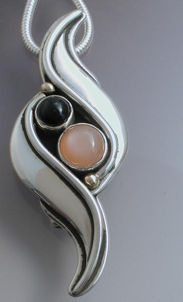 A silver pin/pendant with black onyx and peach colored moonstone picture